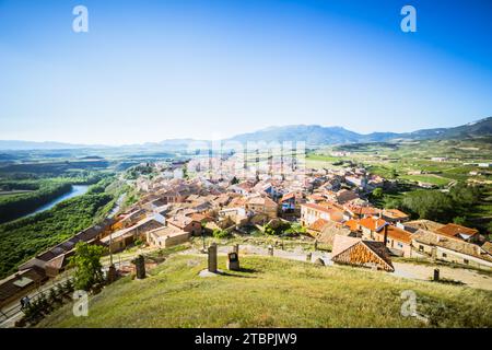 Vista aerea di un piccolo villaggio annidato nella valle di una catena montuosa, con colline ondulate e vegetazione lussureggiante sullo sfondo Foto Stock