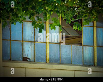 Una vista ravvicinata di una finestra incrinata di un vecchio edificio con pezzi di vetro frantumati sparsi sul davanzale Foto Stock
