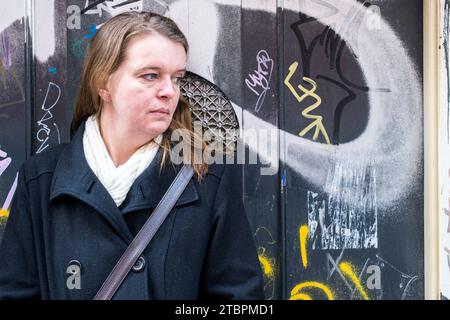 Breda, Paesi Bassi. Ritratto di una donna caucasica media adulta che si lappa contro una porta di legno infestata da graffiti. Foto Stock