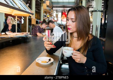 Rotterdam, Paesi Bassi. Ritratto giovane adulto brunette donna seduta a un bar tavola con una tazza di caffè. Foto Stock