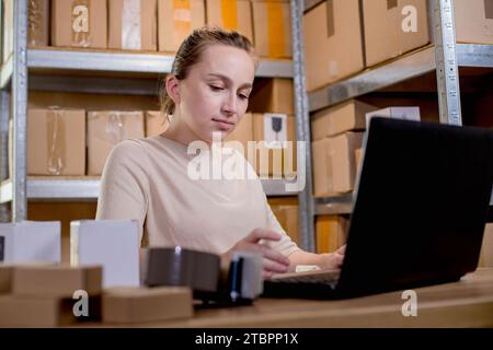 Lavoratrice di magazzino proprietaria di un negozio online che utilizza un computer portatile al lavoro prepara pacchi che controlla le spedizioni di e-commerce vendita al dettaglio online e-commerce Foto Stock