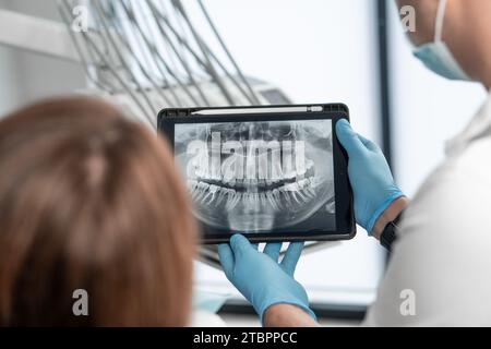 Il dentista mostra i risultati della tomografia panoramica dei denti del paziente su una tavoletta. Il paziente riceve un esame, una consultazione e. Foto Stock