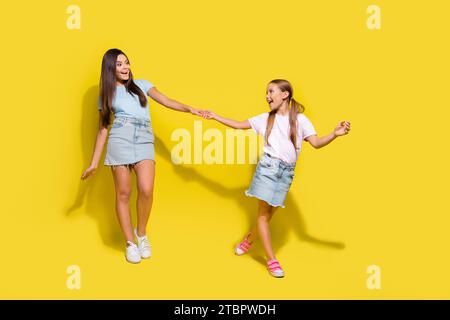 Foto di ragazze positive sorelle più giovani tirano più grandi per comprare giocattoli sul mercato equo isolato su sfondo di colori brillanti Foto Stock