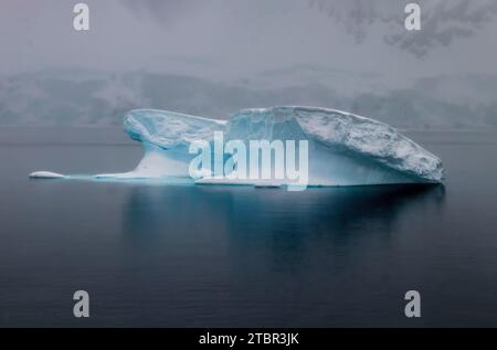 Iceberg in acque calme nei pressi della penisola antartica. Ghiaccio blu; riflesso sull'acqua. Foto Stock