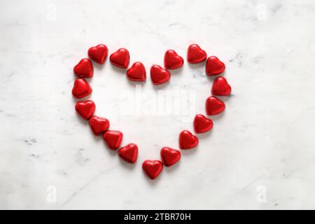 Biglietto d'auguri per San Valentino. Romantico cuore rosso con piccoli dolci di cioccolato rosso come cuore su fondo di marmo bianco. Concetto d'amore. Foto Stock