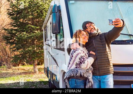 Felice coppia di turisti in camper vanlife che scattano foto di selfie con lo smartphone fuori dal veicolo di viaggio a casa. Concetto di turismo con camper camper camper. Stile di vita alternativo sorride la gente Foto Stock