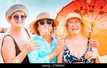 Un gruppo di donne che posano per una foto in estate. Le donne anziane sorridono e godono di una vacanza in stile spiaggia e stile di vita. Le donne anziane sorridono sotto il sole indossano accessori colorati Foto Stock