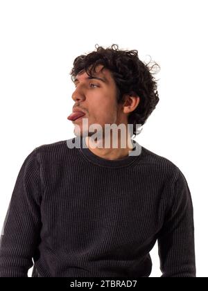 Un uomo che fa una faccia buffa mentre si siede, si sporca la lingua, isolato su sfondo bianco Foto Stock