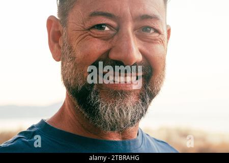 Ritratto ravvicinato di un uomo felice dall'aspetto allegro sulla fotocamera. Un sorriso caucasico adulto maturo con espressione sicura e serena. Sfondo bianco del cielo esterno. Persone ed età felicità stile di vita Foto Stock