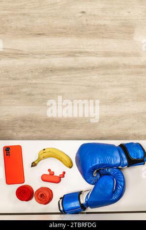 Attrezzatura per Photo Boxing verticale, banana, cuffie e telefono cellulare su una panca nello spogliatoio. Spazio fotocopie pavimento in parquet. Conc. Sport e ricreazione Foto Stock