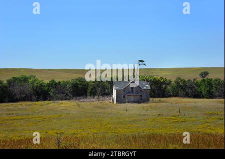 Una casa in pietra deserta si trova sulla prateria aperta del Kansas. La fattoria e' a due piani e in legno. La vernice bianca è incrinata e si stacca,. Foto Stock