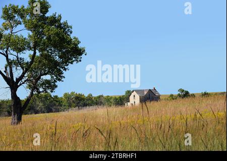 La casa in pietra si trova sulle praterie del Kansas. E' abbandonato ed e' una casa in pietra a due piani. L'erba e i piccoli alberi lo circondano. Foto Stock