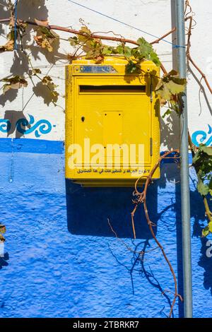 Chefchaouen, Marocco. 14 ottobre 2022 - casella postale gialla marocchina con frase araba appesa accanto a una vite sul muro blu di una casa nel medin Foto Stock