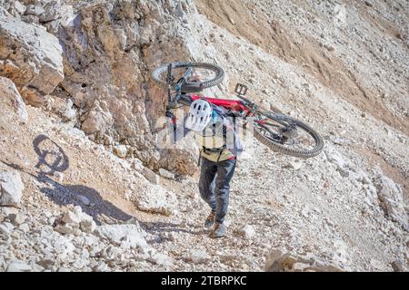 Italia, Dolomiti, ciclista alpinista su un sentiero alpino che porta la mountain bike sulle spalle in un tratto molto difficile Foto Stock