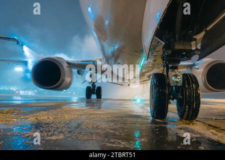 Attenzione selettiva ai meccanismi di atterraggio del velivolo durante lo sbrinamento prima del decollo. Servizio notturno invernale e servizio a terra all'aeroporto. Foto Stock