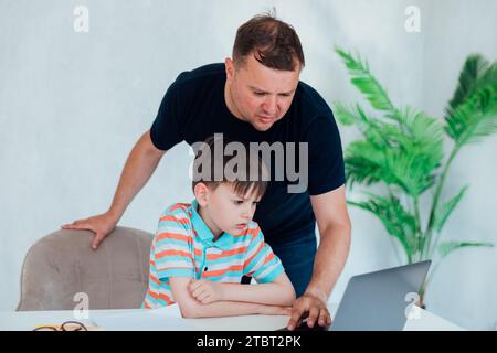 Un insegnante di sesso maschile insegna al bambino a lavorare con un notebook Foto Stock