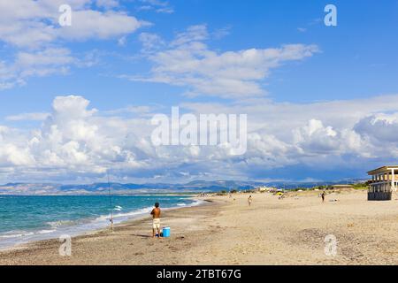 Sulla spiaggia di Plata Mona, Sardegna, Italia, un pescatore sardo è raffigurato con una canna. L'immagine mostra la spiaggia e le montagne lontane. Foto Stock