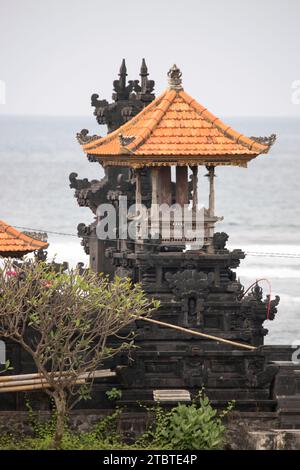 Tempio indù su una spiaggia di sabbia nera vicino al mare, paesaggio serale con onde sul mare su un'isola tropicale a Sanur, Bali, Indonesia Foto Stock