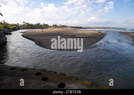 Una spiaggia di sabbia nera direttamente sul mare, splendido paesaggio con onde al tramonto sul mare sull'isola tropicale di Sanur, Bali, Indonesia Foto Stock