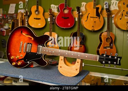 Chitarra elettrica semi-vuota in mostra nel negozio di musica con sottofondo di strumenti assortiti Foto Stock