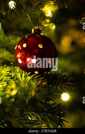 Un ornamento natalizio rosso è appeso al lussureggiante ramo verde di un albero di Natale decorato, creando una splendida scena natalizia Foto Stock