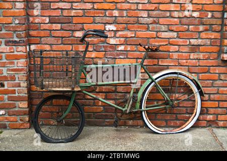 Bicicletta verde d'epoca contro il muro di mattoni rustici in ambientazione urbana Foto Stock