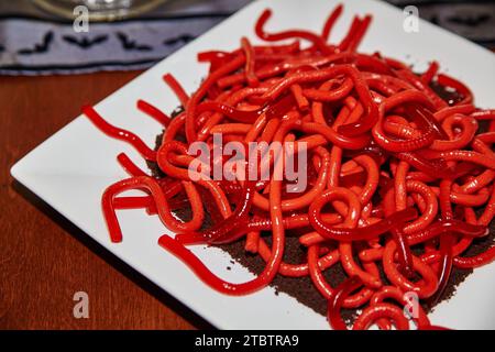 Dessert rosso brillante con verme gommoso su piastra bianca in primo piano Foto Stock