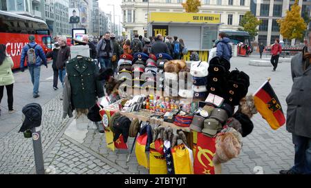 Venditore ambulante di souvenir militari, della Germania dell'Est e sovietici in vendita al Checkpoint Charlie di Berlino, con turisti che passano. Foto Stock