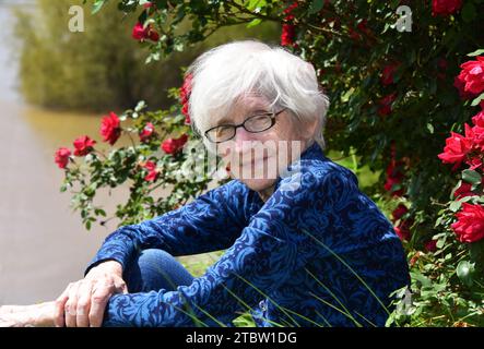 Bella nonna di 99 anni posa sul Camden River Front a Camden, Arkansas. È seduta oltre ad un cespuglio di rose in fiore con l'acqua bel Foto Stock