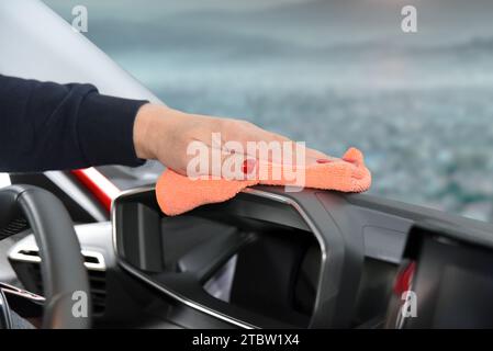 Mano da donna con panno in microfibra per la pulizia della console dell'auto Foto Stock