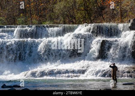 Grande cascata d'acqua del fiume con un pescatore di mosca che guarda in alto. Foto Stock