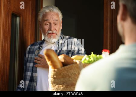 Uomo con un sacco di prodotti in vimini che aiuta il suo vicino più anziano all'aperto Foto Stock