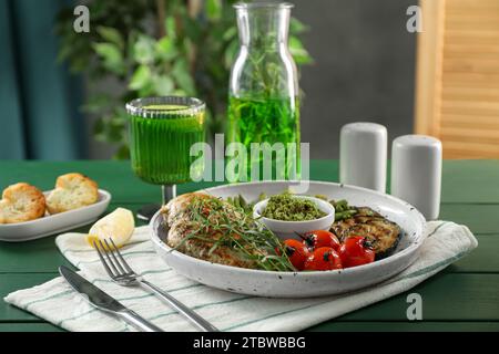 Gustoso pollo, verdure con dragoncello e pesto serviti su un tavolo di legno verde Foto Stock