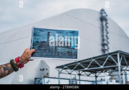 Un'immagine di qualcuno che mostra un'immagine del vecchio sarcofago che proteggeva il quarto reattore della centrale nucleare di Chernobyl davanti al Foto Stock