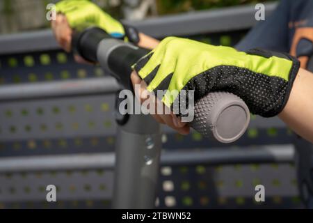 Persona che indossa guanti protettivi in sella a un scooter elettrico in una vista ravvicinata sul manubrio e vivacemente colorato giallo verde guanti Foto Stock