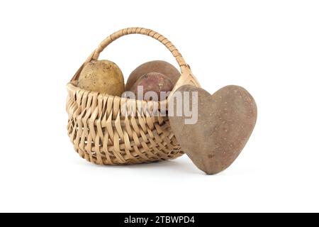 Patate a forma di cuore accanto a un cestino di vimini con patate di vario tipo e colori isolati su sfondo bianco Foto Stock