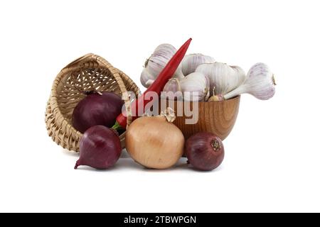 Cipolle rosse e gialle nel cestino di vimini, bulbi d'aglio e spicchi in una ciotola di legno e peperoncino rosso, spezie o condimento a tema ancora vita isolata Foto Stock