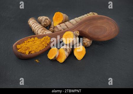 Polvere di curcuma in cucchiaio di legno e rizoma (Curcuma longa Linn) su fondo scuro Foto Stock