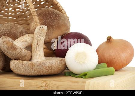 Funghi shiitake freschi, cipolle varie su un tagliere di legno isolato su sfondo bianco. Ricette di funghi ed erbe medicinali Foto Stock