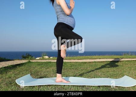 Una donna incinta che fa yoga posa per meditare sulla spiaggia Foto Stock