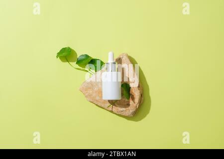 Vista dall'alto di una bottiglia di siero posta su una lastra di pietra con foglie di pennywort fresche. Sfondo pastello per la pubblicità. Concetto di cosmetici naturali con Foto Stock