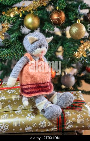 Gattino a maglia seduto su scatole regalo sotto un albero di Natale splendidamente decorato Foto Stock