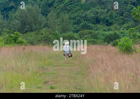 Un uomo asiatico adulto che indossa un cappello con macchina fotografica e treppiede che cammina nel campo di savannah sulla scogliera gigante, sulla spiaggia di Hat Thai Mueng, nella provincia di Phangnga. Sustainab Foto Stock