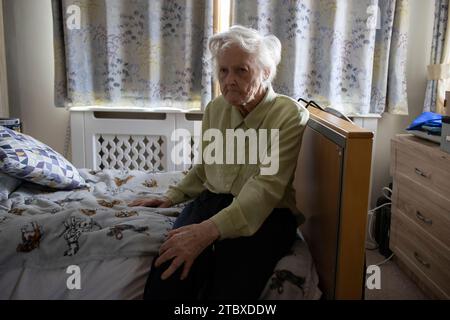 Anziana signora di 80 anni siede da sola nella sua camera da letto di casa di assistenza sociale, Inghilterra, Regno Unito Foto Stock