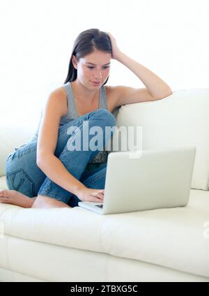 Divano, laptop e donna o studente per Internet, formazione online o ricerca di informazioni di iscrizione sul sito Web. I giovani si rilassano sul divano e scrivono Foto Stock