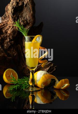 Liquore tradizionale italiano Limoncello su sfondo nero riflettente. Bicchiere di liquore al limone con ramoscello di rosmarino su sfondo di vecchio serpente. Foto Stock