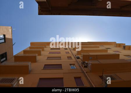 Lato di un condominio dipinto di giallo con balconi, finestre e unità di aria condizionata in una stradina nel centro di Trapani, Sicilia Foto Stock