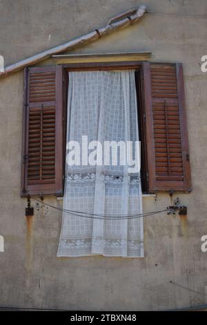 Tenda bianca ricamata appesa attraverso la finestra con persiane aperte in legno marrone Foto Stock