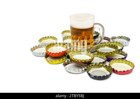 I tappi delle bottiglie di birra in metallo incorniciano il gruppo isolato su bianco. In cima c'è una tazza da birra decorativa. Immagine concettuale del consumo di alcol. Foto Stock