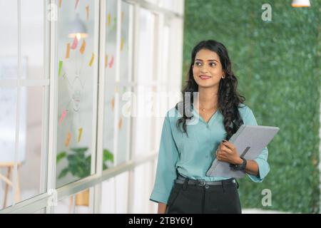 Accompagnare con sicurezza una giovane donna d'affari in ufficio con un notebook - concetto di dipendente aziendale di successo, crescita professionale e motivazione. Foto Stock